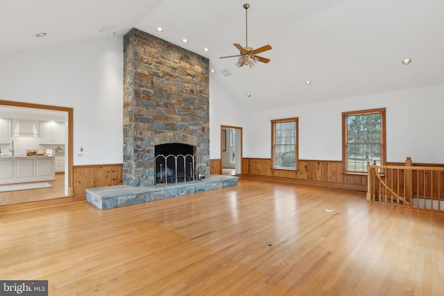 unfurnished living room featuring a wainscoted wall, high vaulted ceiling, a stone fireplace, and wood finished floors