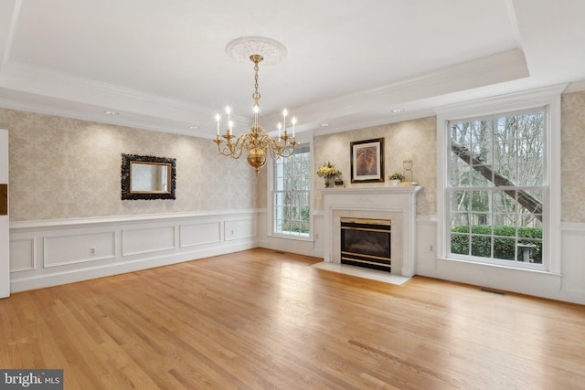 unfurnished living room with wallpapered walls, a wainscoted wall, a premium fireplace, wood finished floors, and a raised ceiling