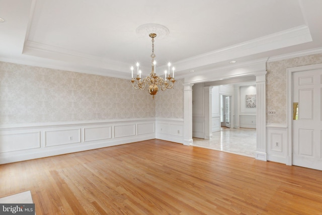 empty room featuring a wainscoted wall, light wood-style flooring, wallpapered walls, and a tray ceiling