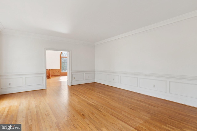 spare room with light wood-style floors, ornamental molding, and wainscoting