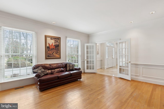 living area featuring visible vents, ornamental molding, wood finished floors, french doors, and a decorative wall