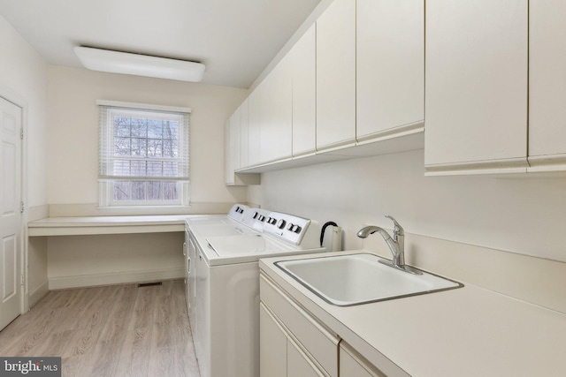 washroom with baseboards, light wood finished floors, cabinet space, a sink, and washing machine and dryer