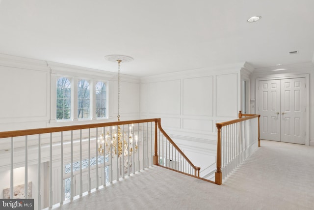 hallway featuring ornamental molding, an upstairs landing, carpet flooring, an inviting chandelier, and a decorative wall