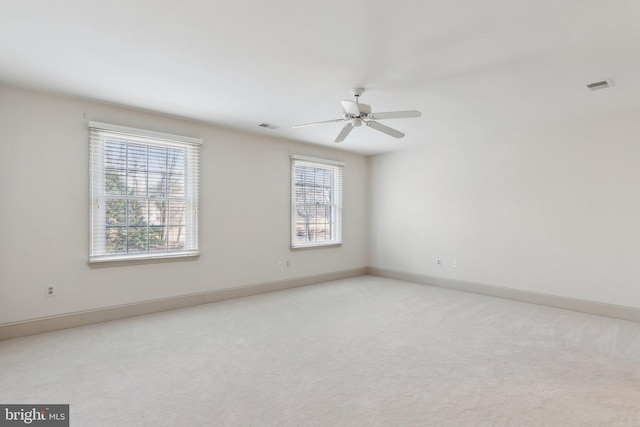 empty room featuring visible vents, light carpet, baseboards, and a ceiling fan