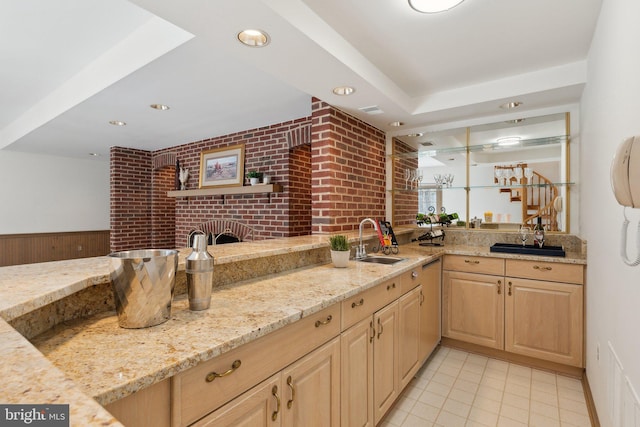 kitchen with brick wall, light brown cabinetry, light stone counters, recessed lighting, and a sink