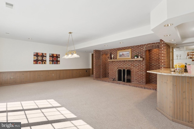 unfurnished living room with carpet, visible vents, a fireplace, wood walls, and wainscoting