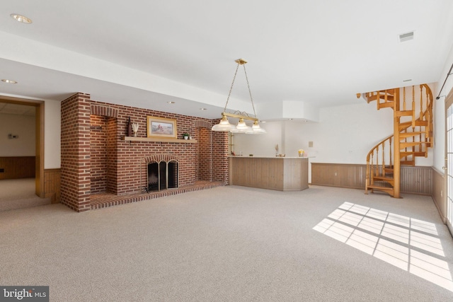 unfurnished living room featuring carpet, visible vents, a wainscoted wall, a fireplace, and stairs