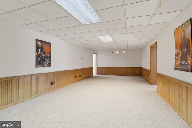 finished below grade area featuring wooden walls, wainscoting, visible vents, and a drop ceiling