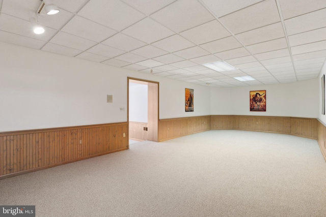 basement with carpet flooring, wainscoting, a paneled ceiling, and wood walls