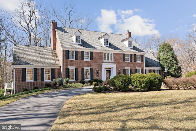 georgian-style home with aphalt driveway, a front yard, brick siding, and a chimney