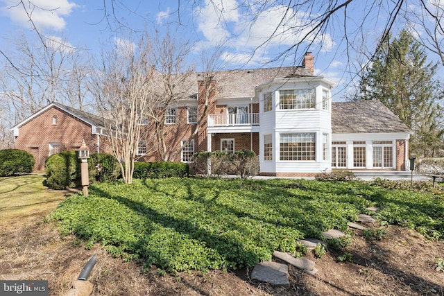 view of front of house featuring a front yard, brick siding, a balcony, and a chimney