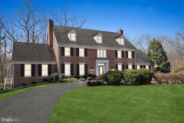 colonial inspired home featuring brick siding, driveway, a chimney, and a front yard