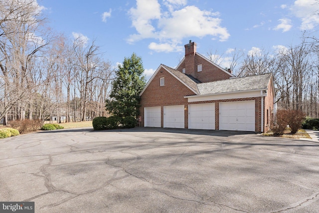 view of side of property with a garage, brick siding, and a chimney