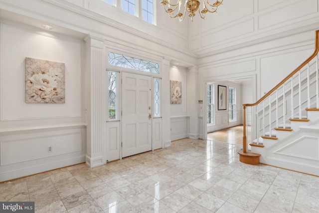 foyer entrance featuring a towering ceiling, stairway, crown molding, a decorative wall, and a chandelier