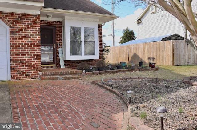 exterior space featuring brick siding, a garage, roof with shingles, and fence