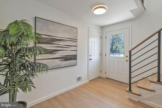 entryway featuring visible vents, baseboards, wood finished floors, and stairs