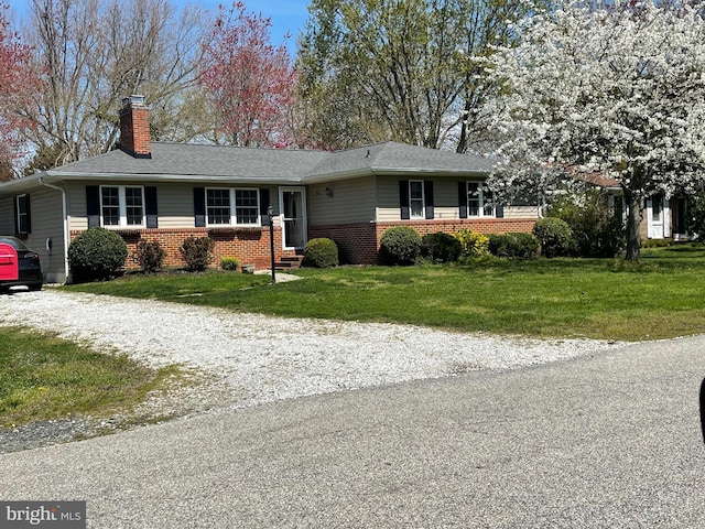 ranch-style home featuring gravel driveway, a front lawn, brick siding, and a chimney