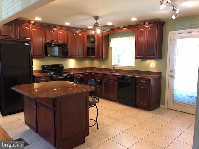 kitchen with a center island, ceiling fan, light tile patterned floors, a kitchen breakfast bar, and black appliances