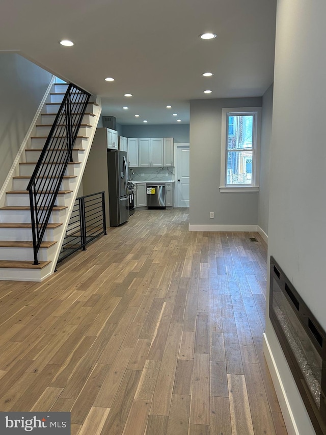 unfurnished living room featuring recessed lighting, stairway, baseboards, and light wood-style flooring