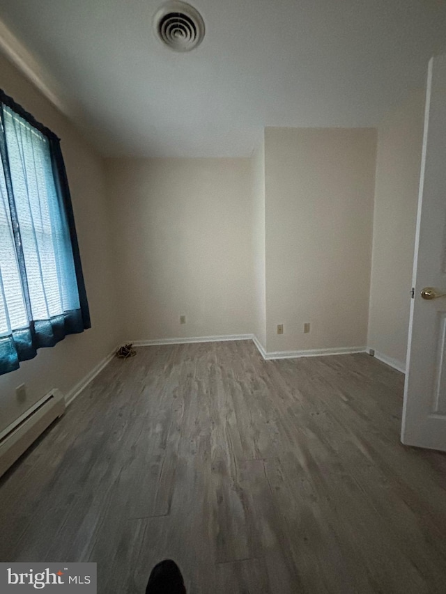 unfurnished room featuring visible vents, baseboards, baseboard heating, and wood finished floors