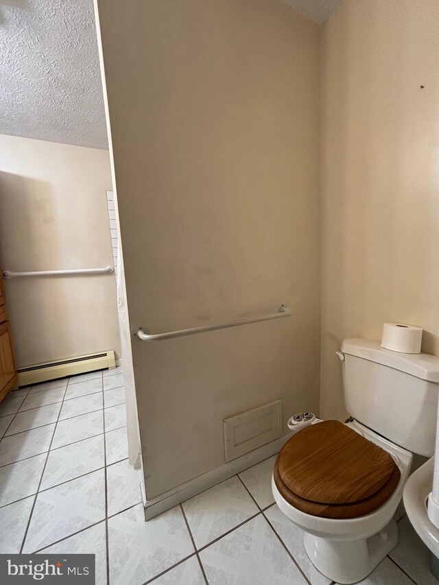 bathroom featuring tile patterned flooring, toilet, a baseboard heating unit, and a textured ceiling