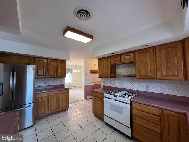 kitchen featuring freestanding refrigerator, white range with gas stovetop, visible vents, dark countertops, and brown cabinets