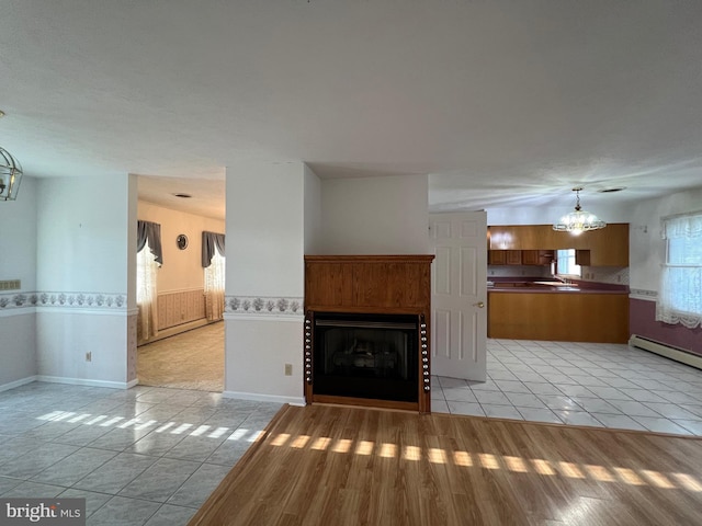 unfurnished living room with an inviting chandelier, a sink, a fireplace, a wainscoted wall, and light tile patterned flooring