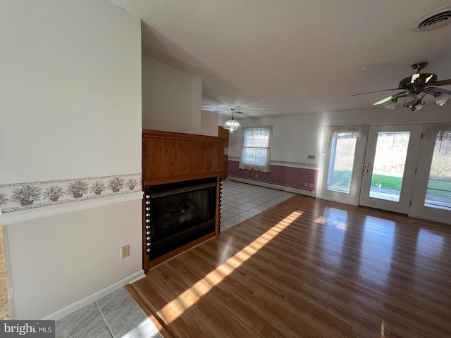 unfurnished living room featuring baseboards, a fireplace, visible vents, a baseboard radiator, and ceiling fan with notable chandelier