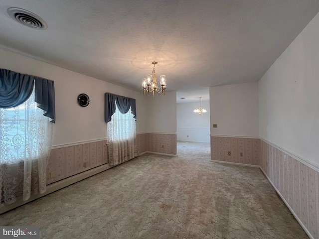 spare room featuring a chandelier, carpet flooring, wainscoting, and visible vents
