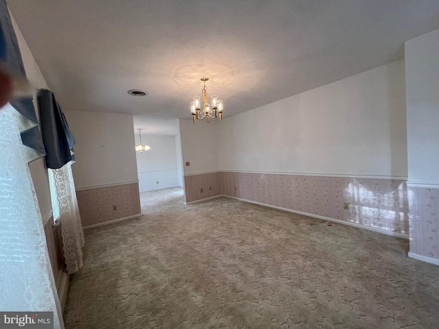 empty room featuring wallpapered walls, a chandelier, a wainscoted wall, carpet floors, and visible vents