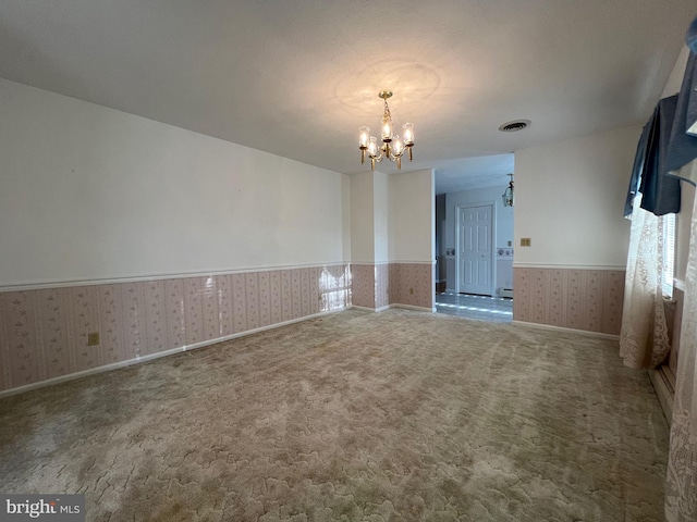 carpeted spare room with visible vents, baseboards, a chandelier, wallpapered walls, and a wainscoted wall