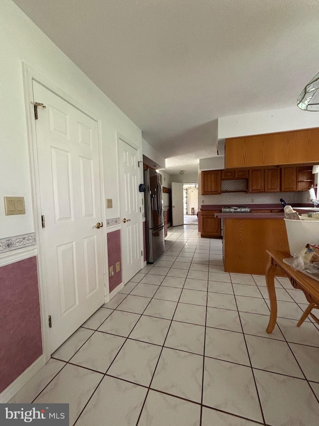 kitchen featuring stainless steel fridge with ice dispenser, light tile patterned floors, a peninsula, brown cabinetry, and decorative backsplash