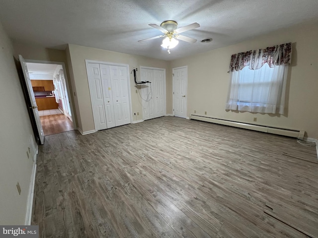 unfurnished bedroom featuring a baseboard radiator, two closets, wood finished floors, and baseboards