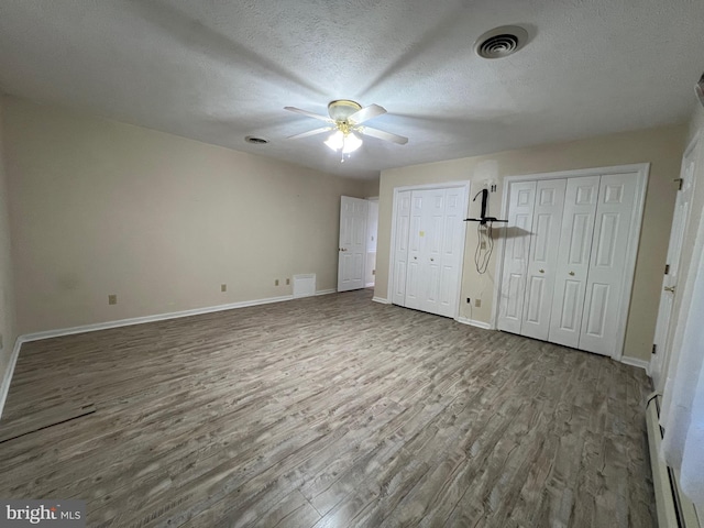 unfurnished bedroom with wood finished floors, baseboards, and multiple closets