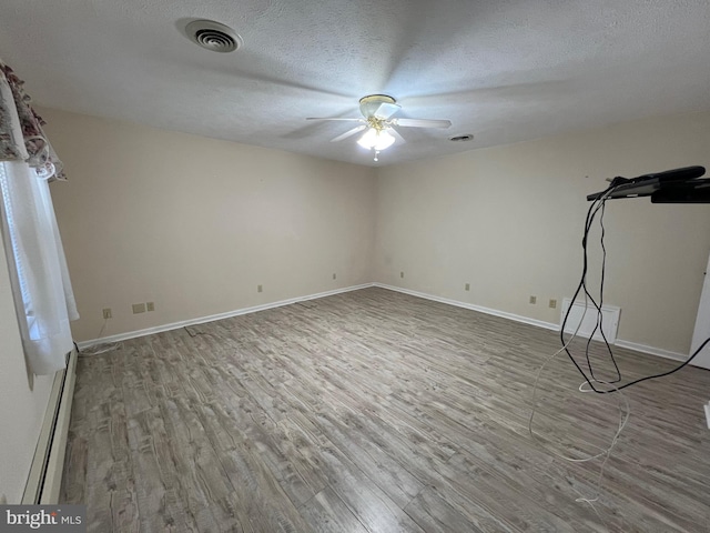 spare room featuring visible vents, a baseboard heating unit, a ceiling fan, and wood finished floors