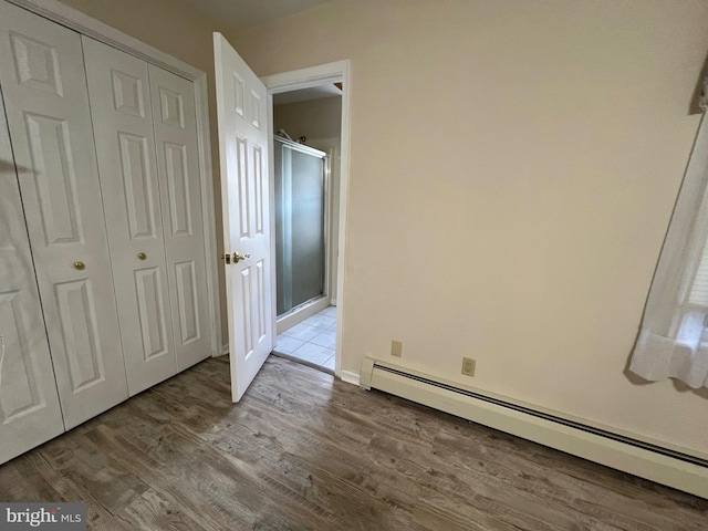 unfurnished bedroom featuring baseboard heating, wood finished floors, a closet, and baseboards