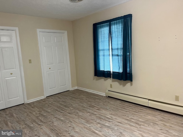 unfurnished bedroom with a textured ceiling, wood finished floors, a baseboard heating unit, and baseboards