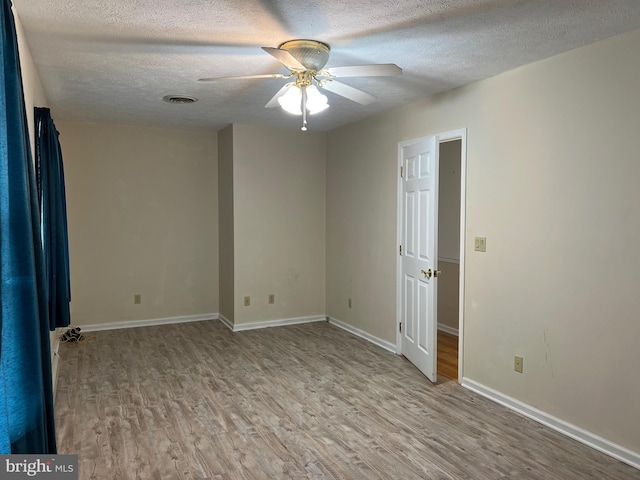 empty room with ceiling fan, a textured ceiling, visible vents, wood finished floors, and baseboards