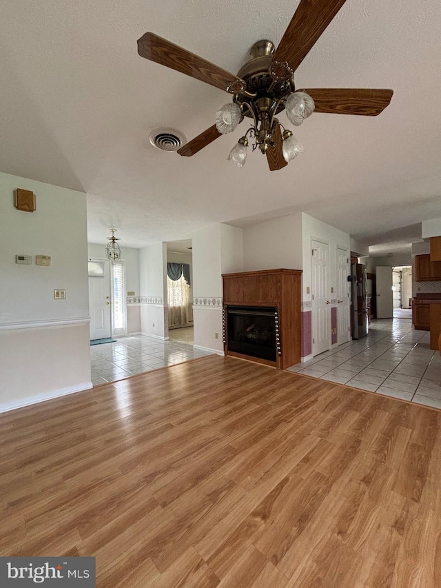 unfurnished living room with baseboards, light wood-type flooring, a ceiling fan, visible vents, and a tile fireplace