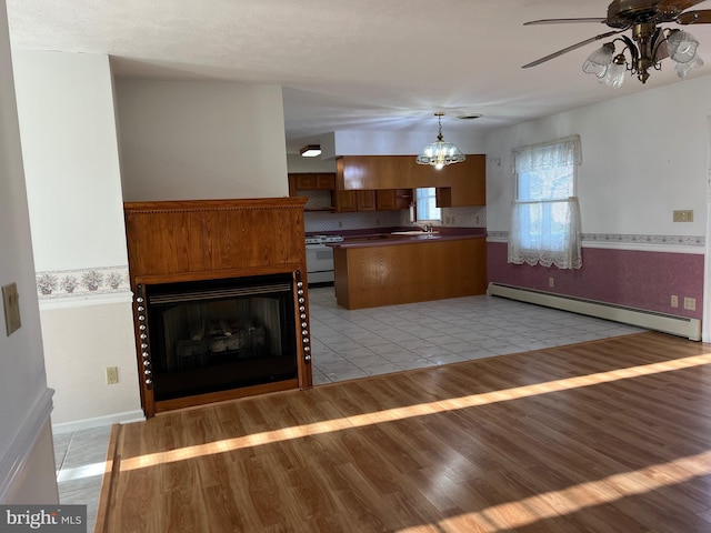 kitchen featuring a baseboard heating unit, white electric stove, brown cabinets, ceiling fan with notable chandelier, and a sink