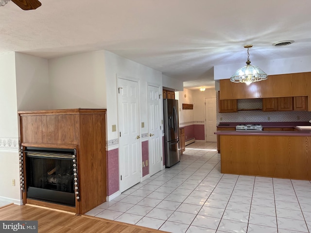 kitchen featuring stainless steel fridge, decorative light fixtures, a peninsula, brown cabinetry, and stove