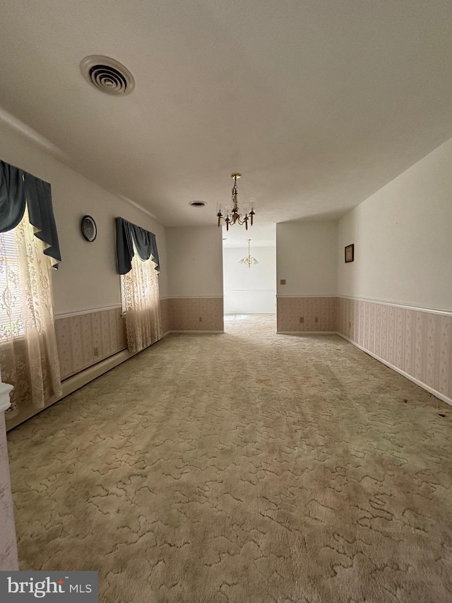 unfurnished dining area with visible vents, a wainscoted wall, an inviting chandelier, and carpet floors