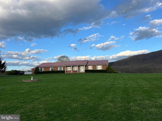 rear view of house with brick siding, a mountain view, metal roof, and a lawn