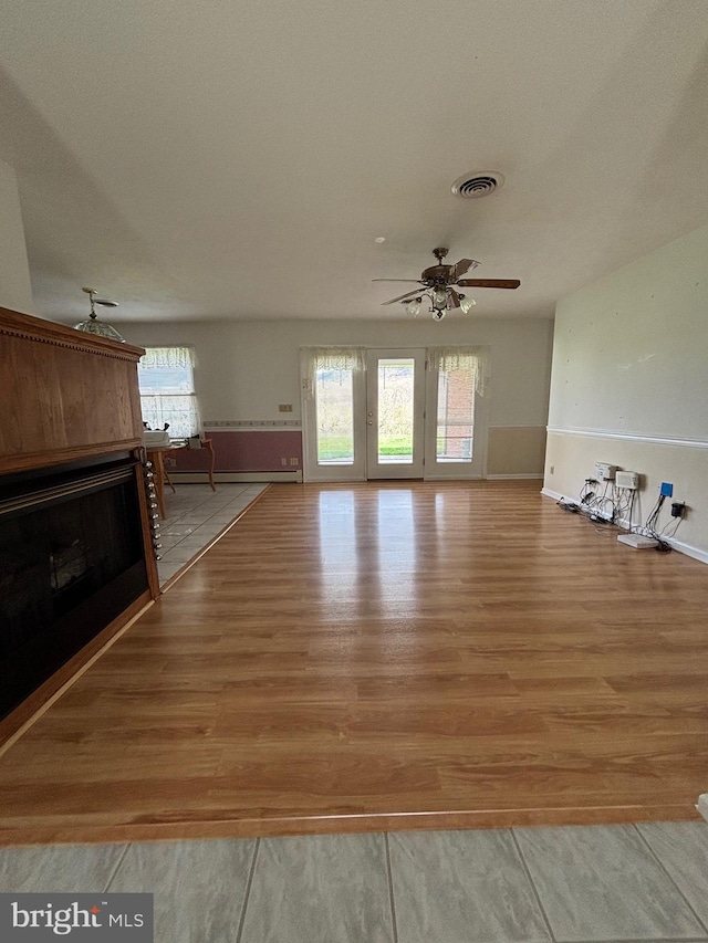 unfurnished living room with visible vents, light wood-style flooring, ceiling fan, and baseboards