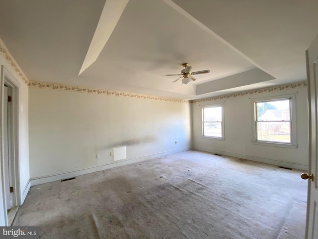 empty room featuring a tray ceiling, light carpet, and baseboards