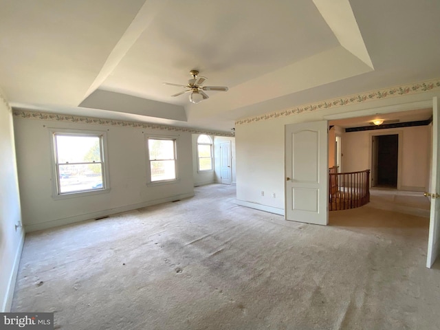 interior space with light carpet, ceiling fan, a raised ceiling, and baseboards