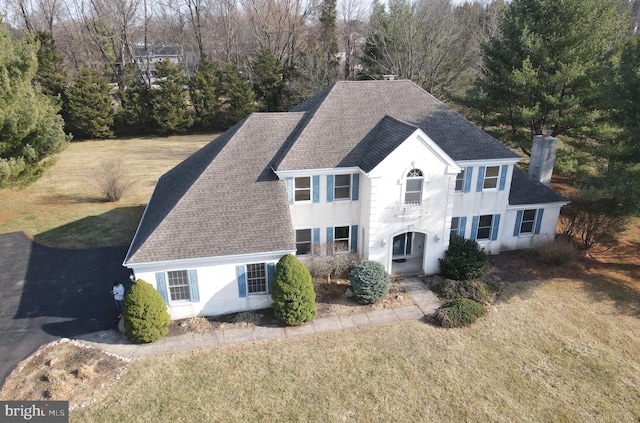 view of front facade featuring a front lawn, stucco siding, roof with shingles, and a chimney