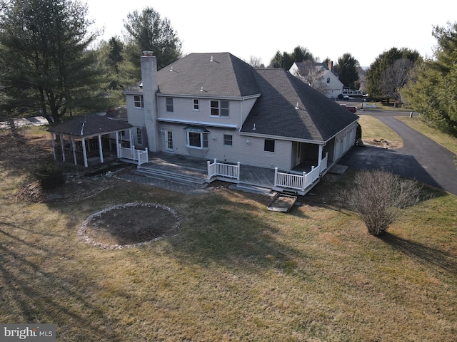 rear view of house featuring a deck, a yard, roof with shingles, and a chimney