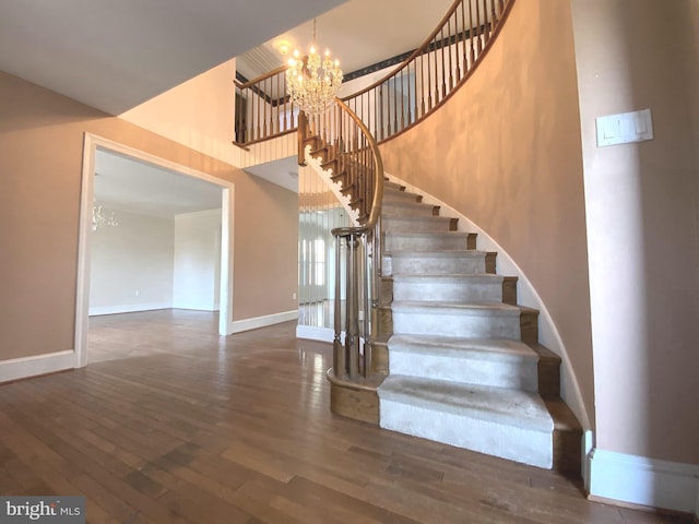 stairway with baseboards, wood finished floors, a high ceiling, and a chandelier