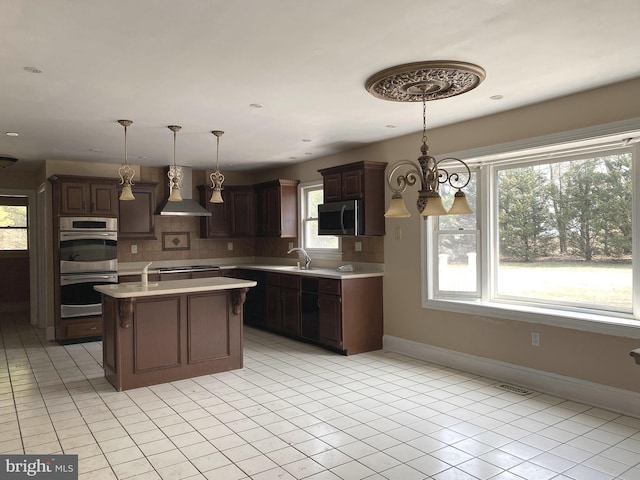 kitchen with light countertops, decorative backsplash, stainless steel appliances, wall chimney exhaust hood, and a sink